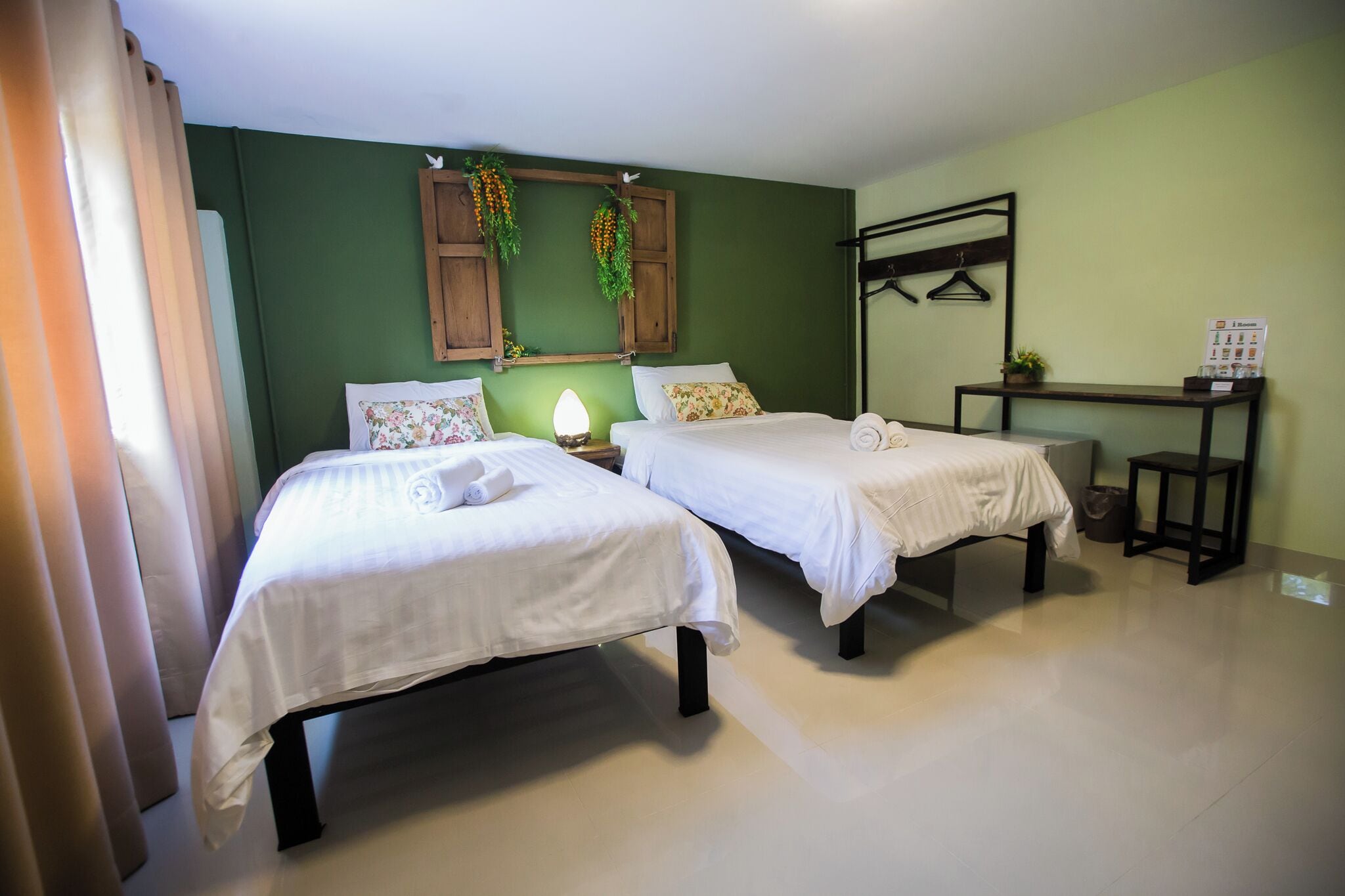 A room with two beds, a desk, and a hanging plant.