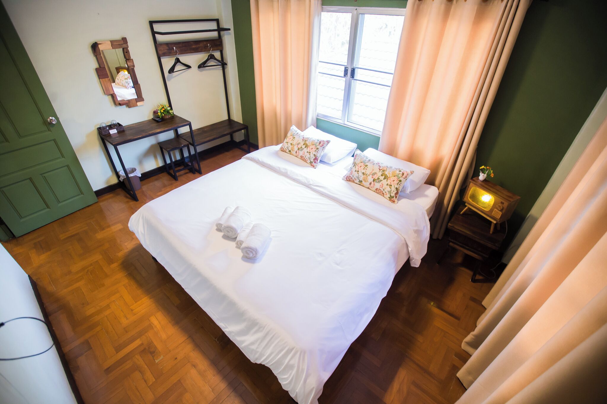 Una cama bien hecha con almohadas y toallas, una mesita de noche con lámpara, un espejo y una ventana con cortinas.