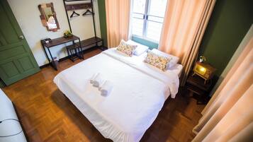 A neatly made bed with pillows and towels, a bedside table with a lamp, a mirror, and a window with curtains.