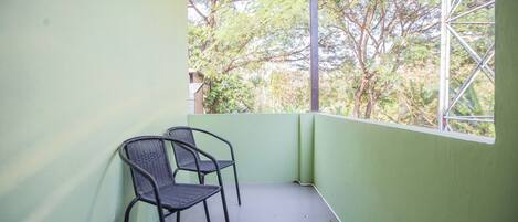 Un balcón con dos sillas, un muro verde y vistas a árboles y un edificio.