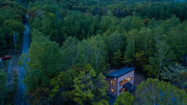 A modern house surrounded by dense forest with a mountain in the background. - Forest Hideaway (Niseko)