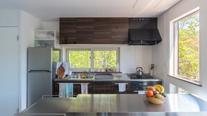 A modern kitchen with a large island, stainless steel appliances, and a view of trees through the window. - Forest Hideaway (Niseko)