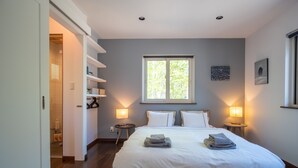 A bedroom with a large bed, two bedside lamps, a window with a view, and a door leading to a bathroom. - Forest Hideaway (Niseko)