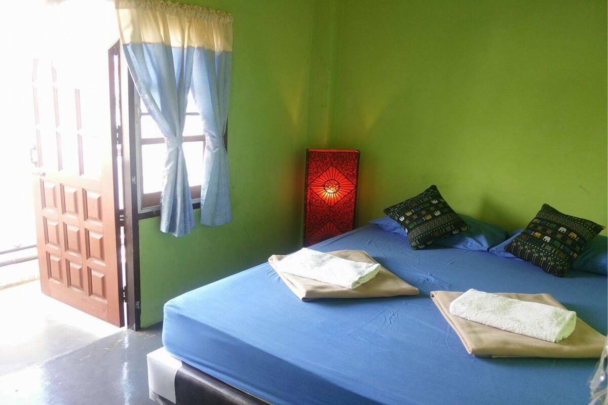 A room with a bed, a red decorative item on the wall, and a door with curtains.