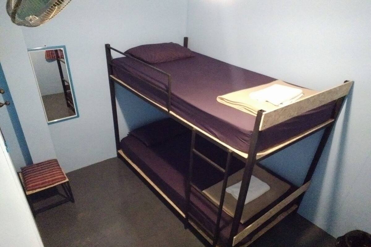 A bunk bed room with a mirror, a small stool, and a fan.