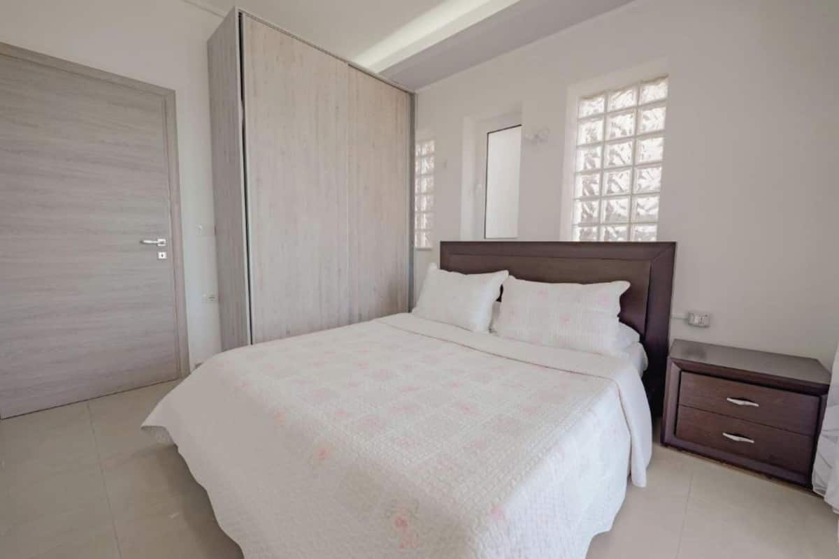 A bedroom with a bed, a wardrobe, a nightstand, and a window with a view.