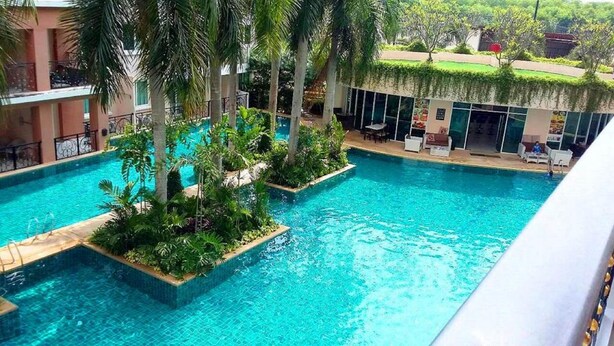 A swimming pool with surrounding greenery and a building with a covered patio area. - Paradise Park (Pattaya)