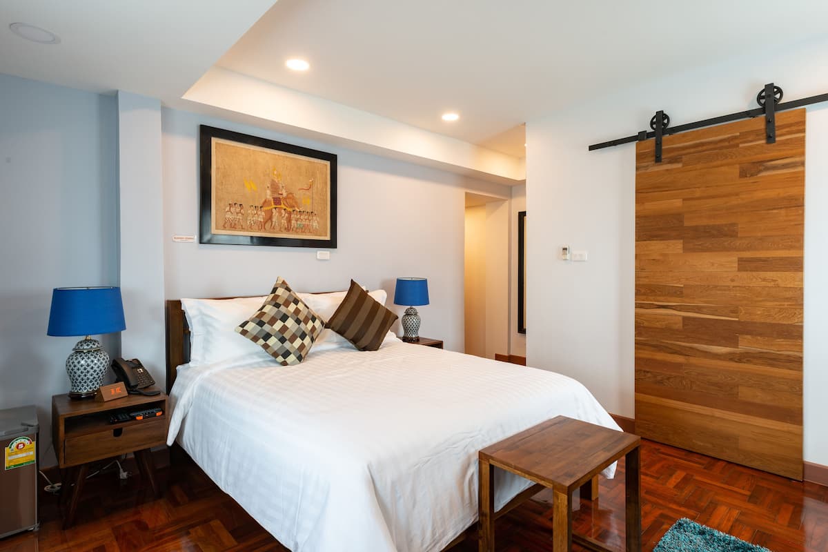 A neatly arranged bedroom with a bed, bedside tables, a lamp, a framed picture, and a wooden sliding door.