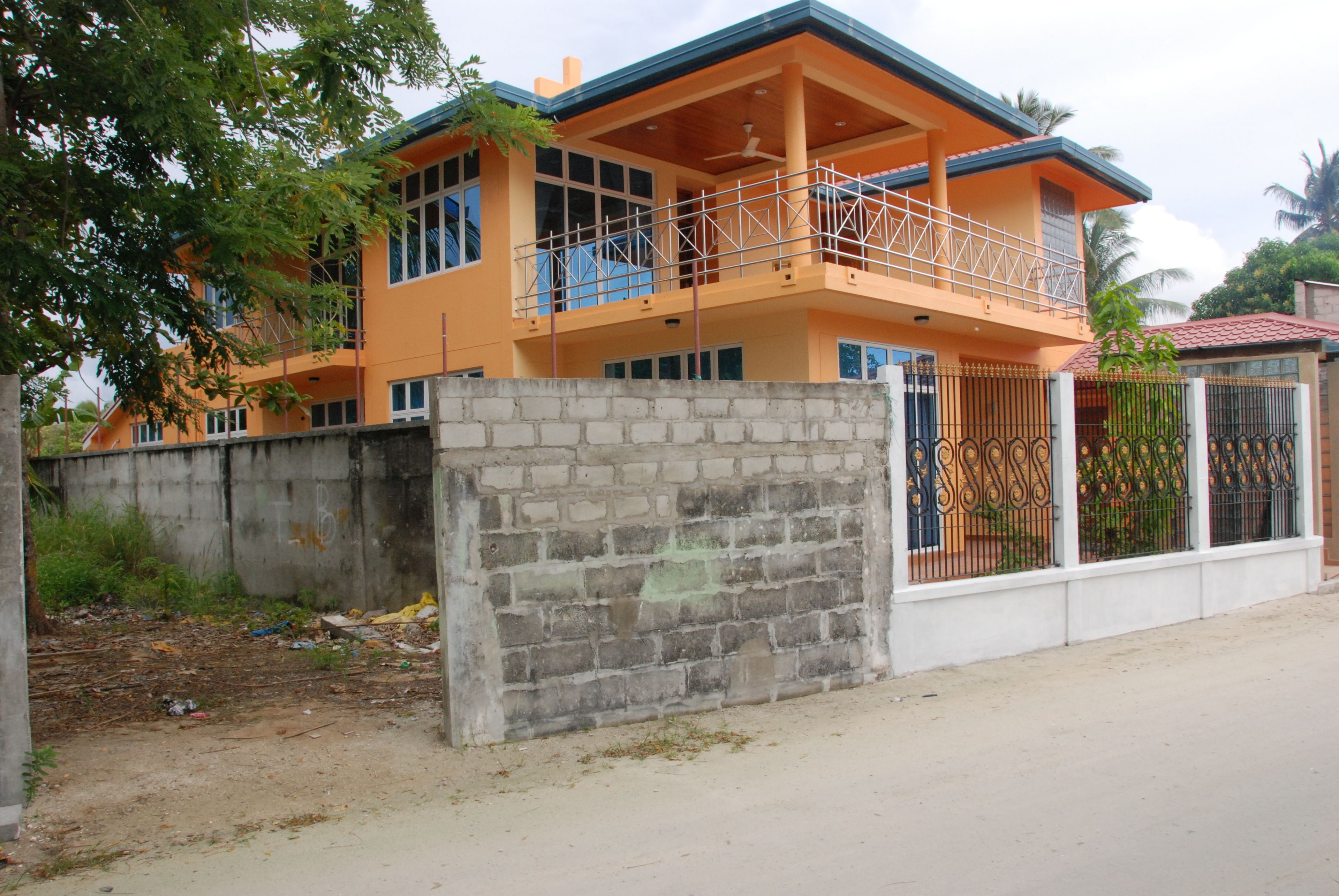 A two-story house with a balcony, a brick wall in front, and a metal gate.