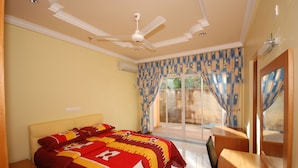 Un dormitorio con cama, ventilador de techo, ventana con cortinas y vistas al exterior.