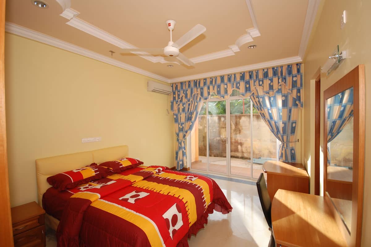 Quarto com cama, ventoinha no teto, janela com cortinas e vista para o exterior.