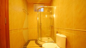 Un baño con cabina de ducha de vidrio, inodoro y paredes de azulejos amarillos.