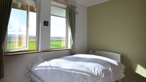 A bedroom with a large bed, a window with curtains, a view of the outdoors, and a ceiling with exposed beams. - Gufo no Mori Kamifurano (Kamifurano)