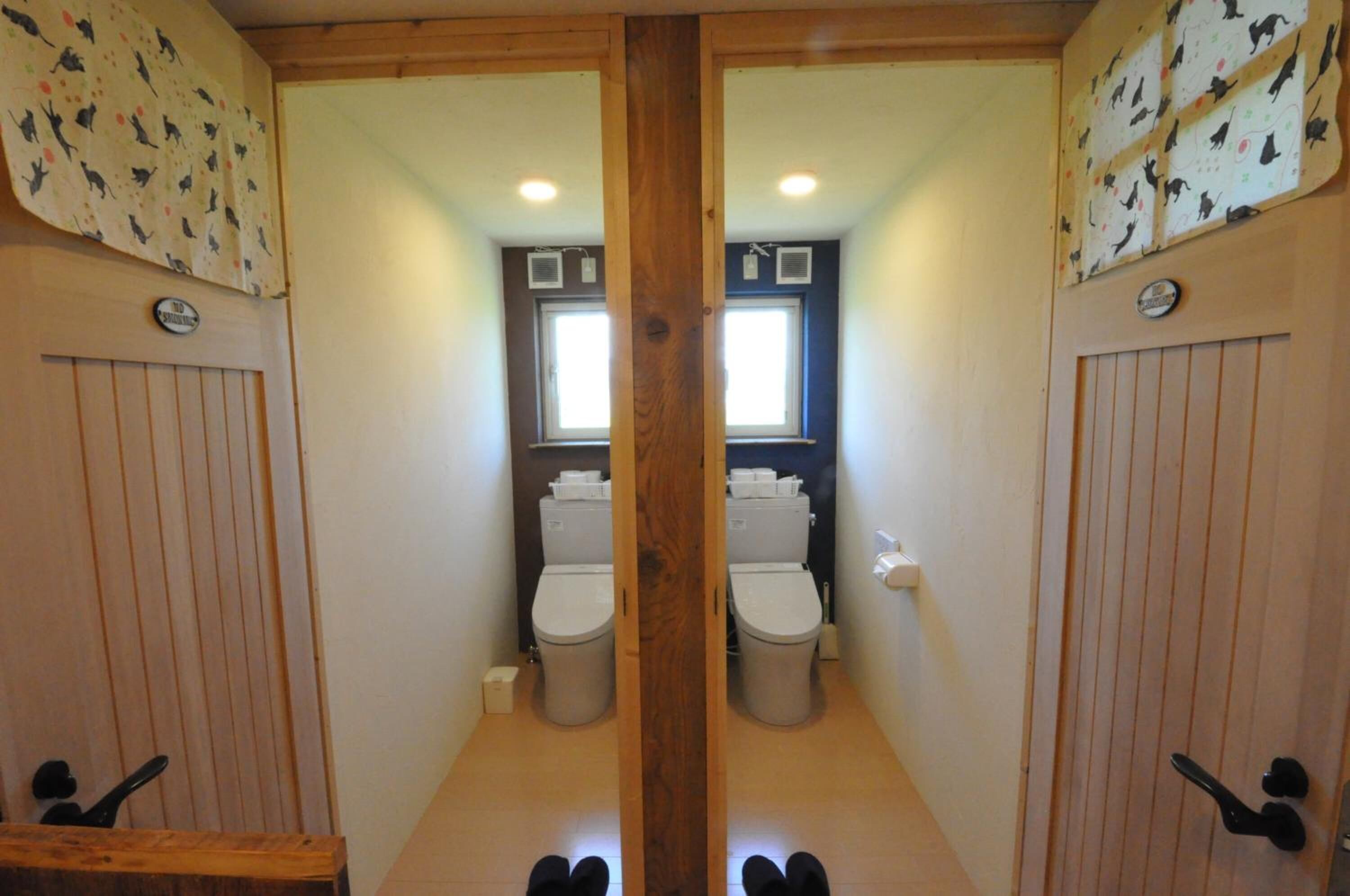 A mirrored bathroom with two toilets, a window, and wooden paneling.