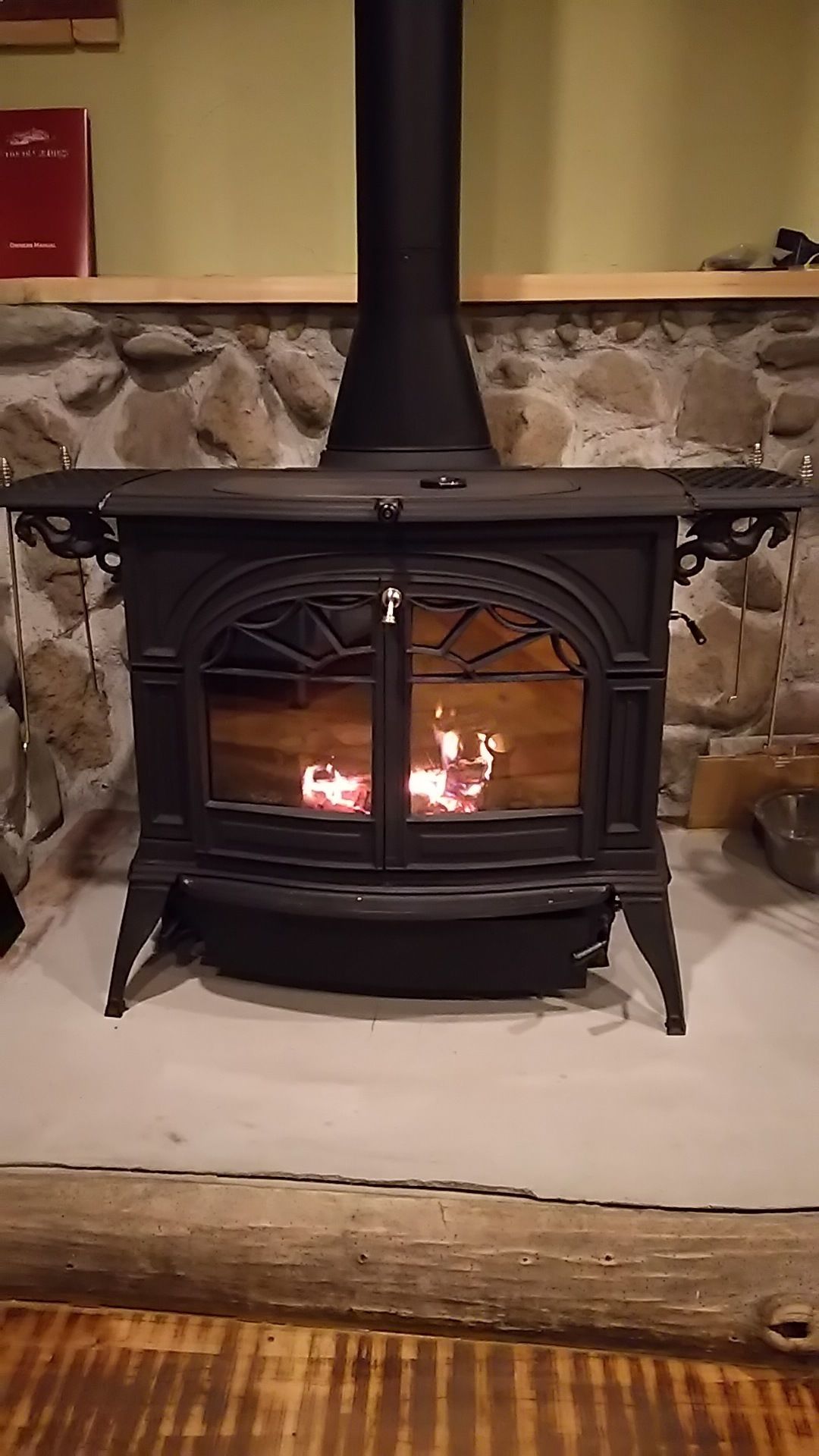 A wood-burning stove with a stone wall background and a wooden floor.