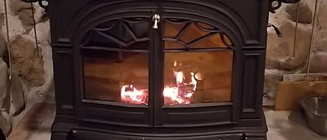 A wood-burning stove with a stone wall background and a wooden floor.