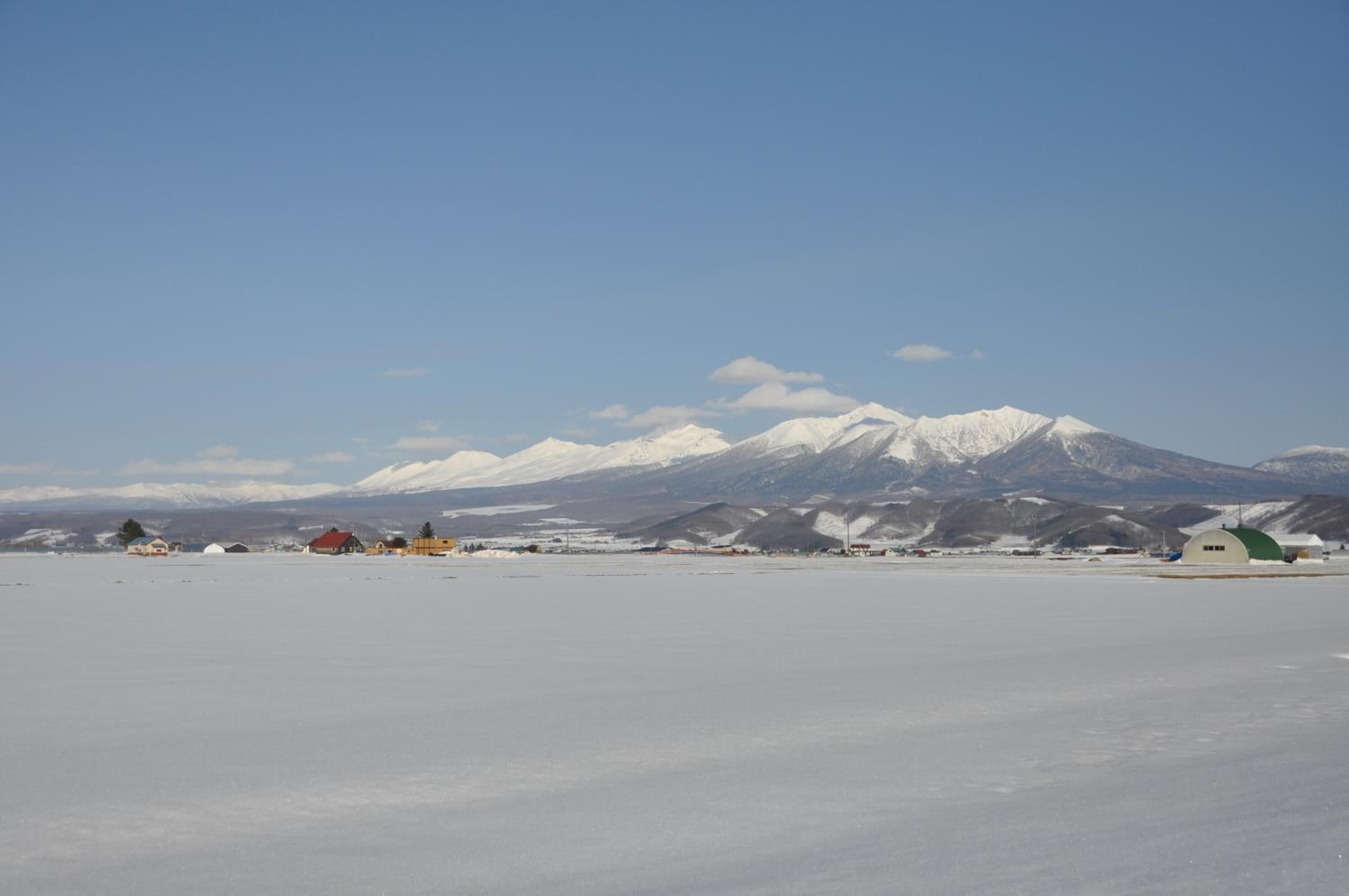 A snowy landscape with a mountain range in the background and several buildings with red and green roofs.