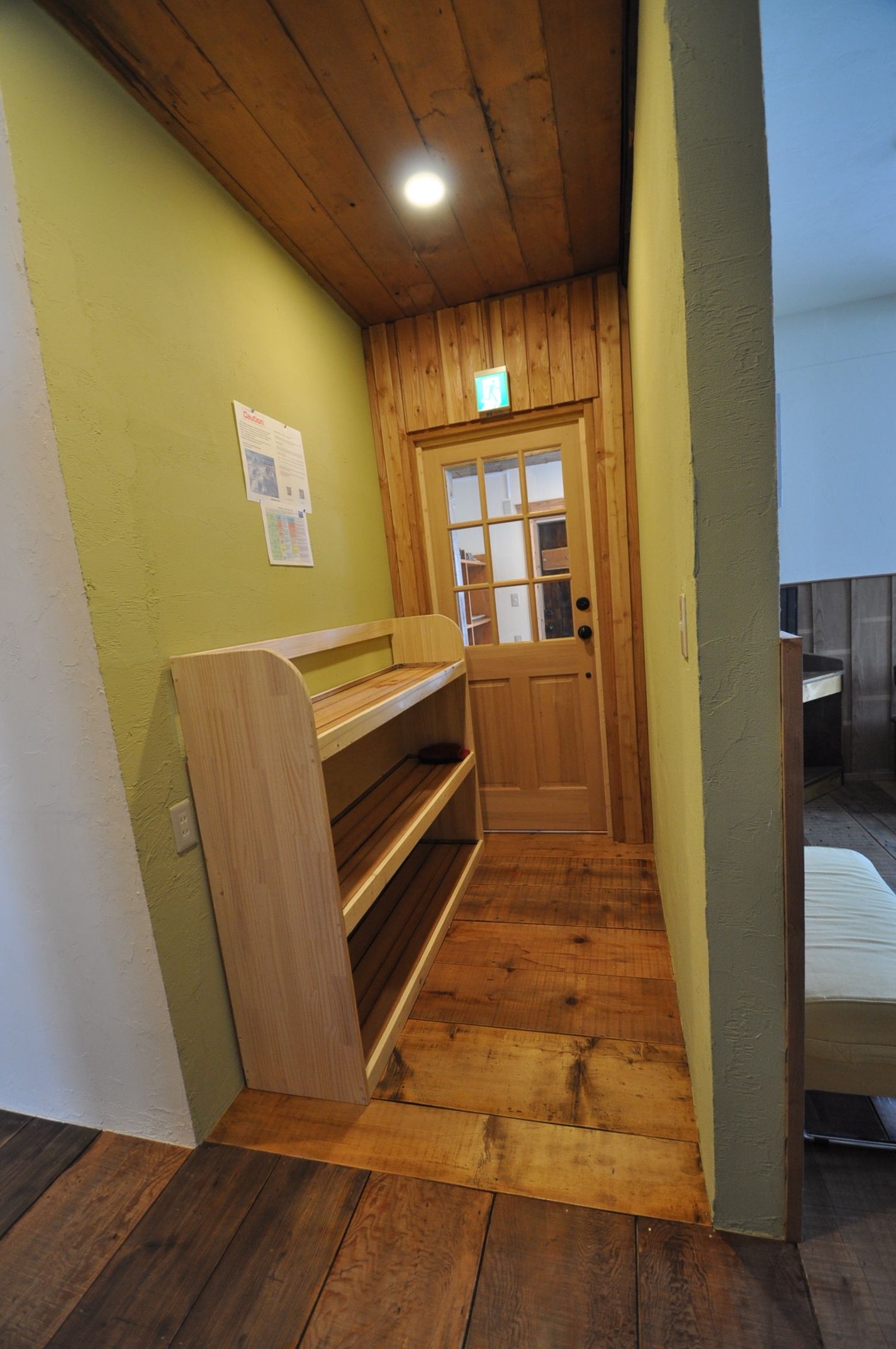 A narrow hallway with wooden flooring and a wooden bench. A door with glass panels and a small window is visible in the background.