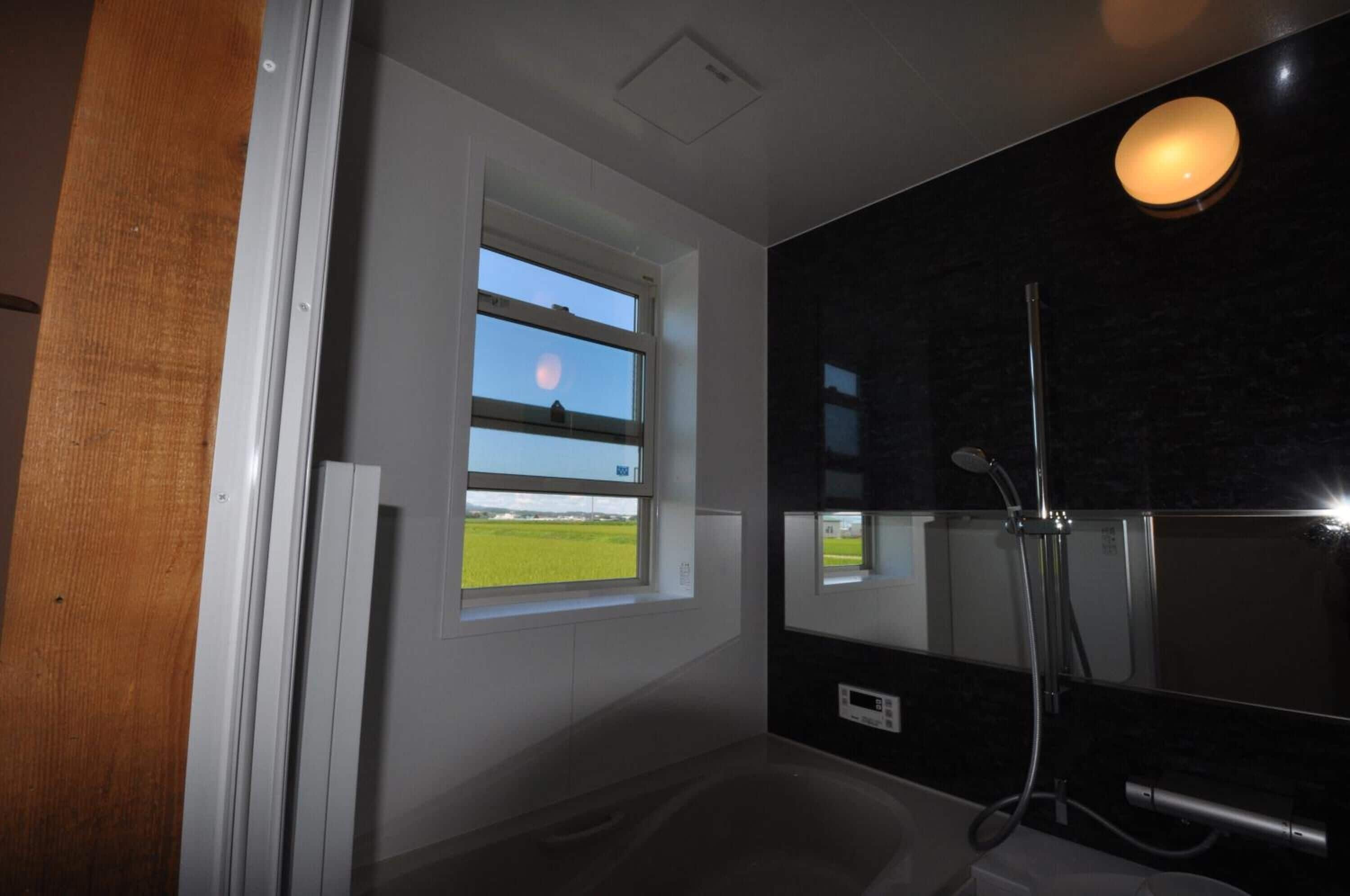 A modern bathroom with a bathtub, a shower, and a window with a view of a field and the moon.