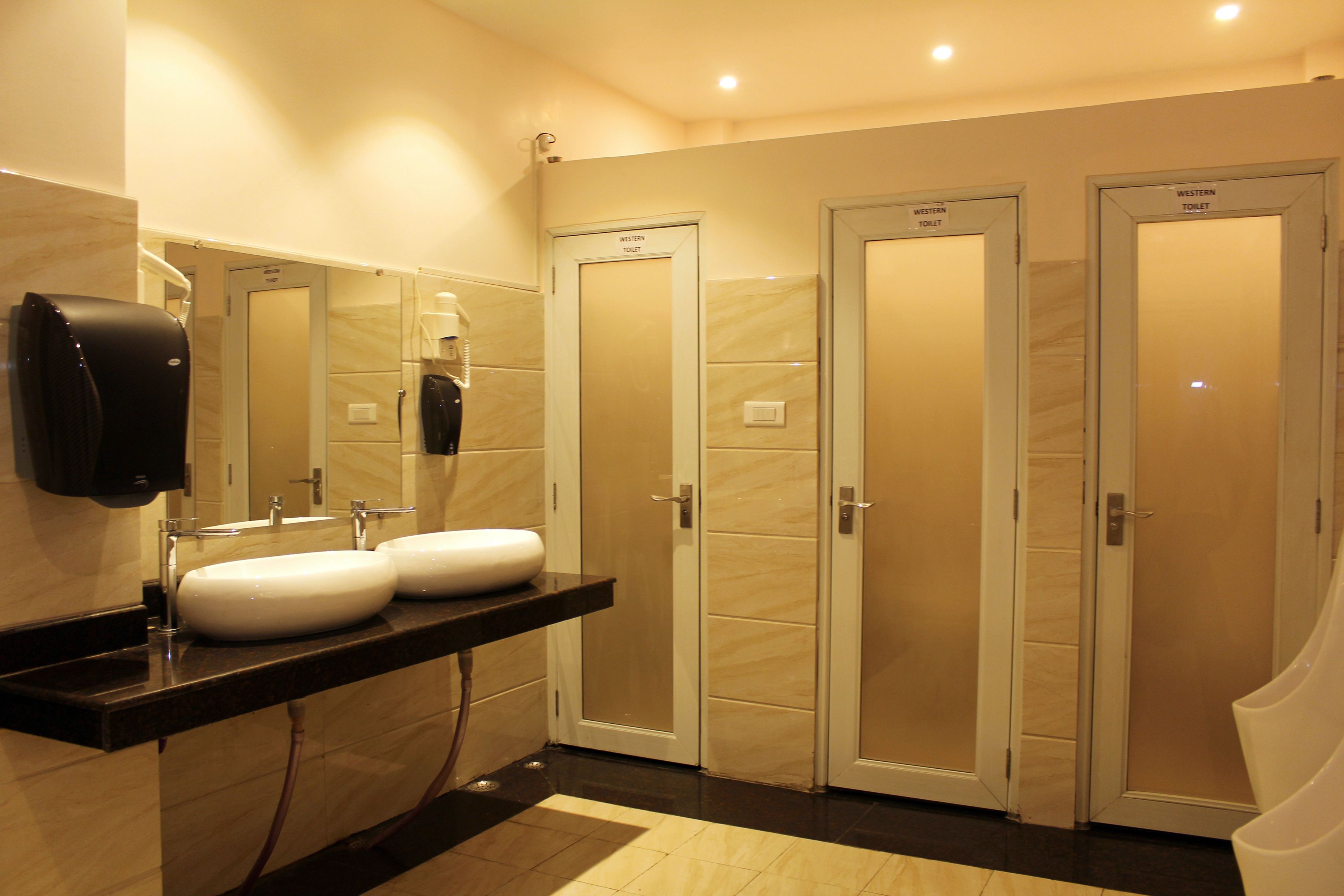 A hotel bathroom with two sinks, a hand dryer, and three Western toilets.