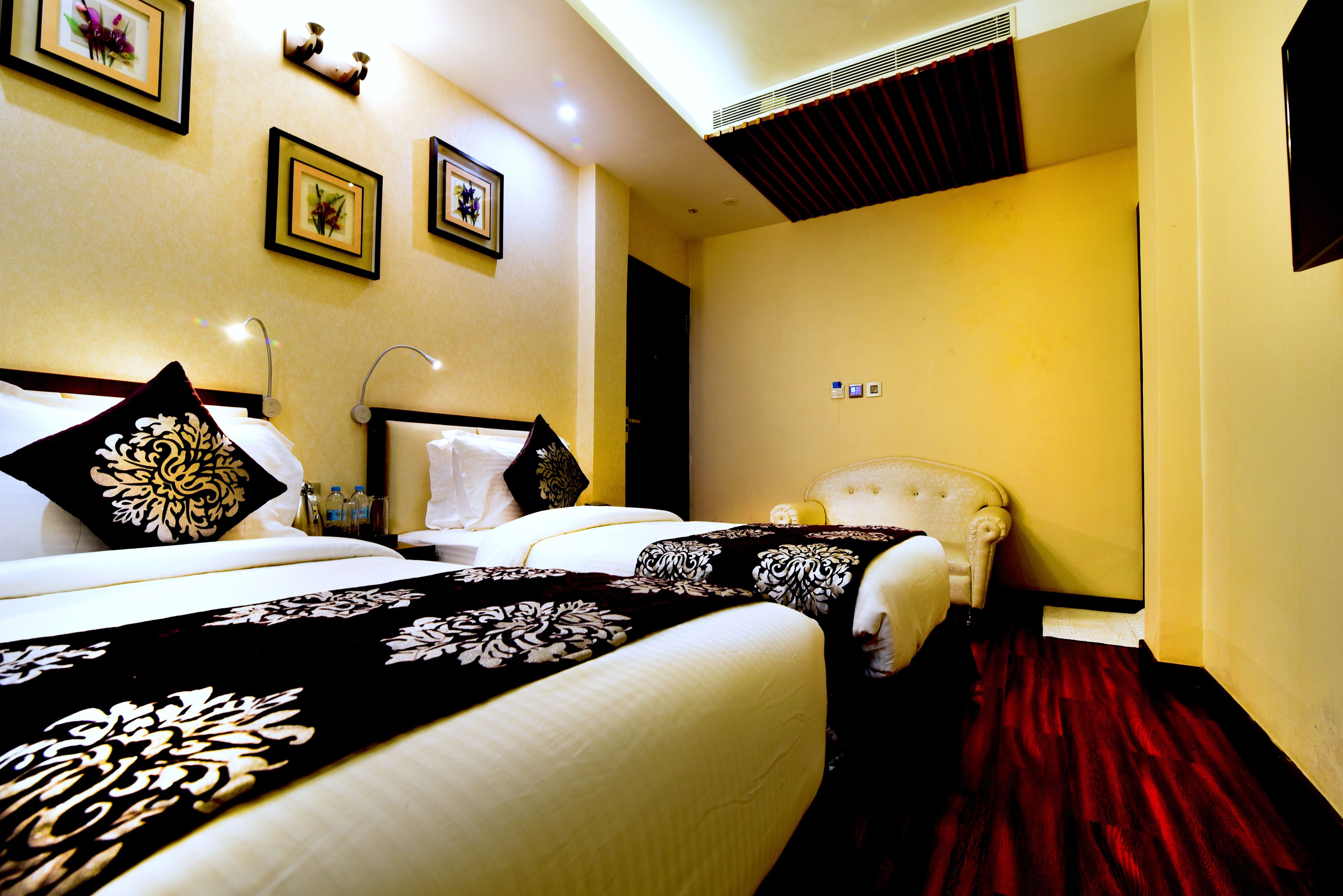 A hotel room with a large bed, a smaller bed, a red carpet, and framed pictures on the wall.