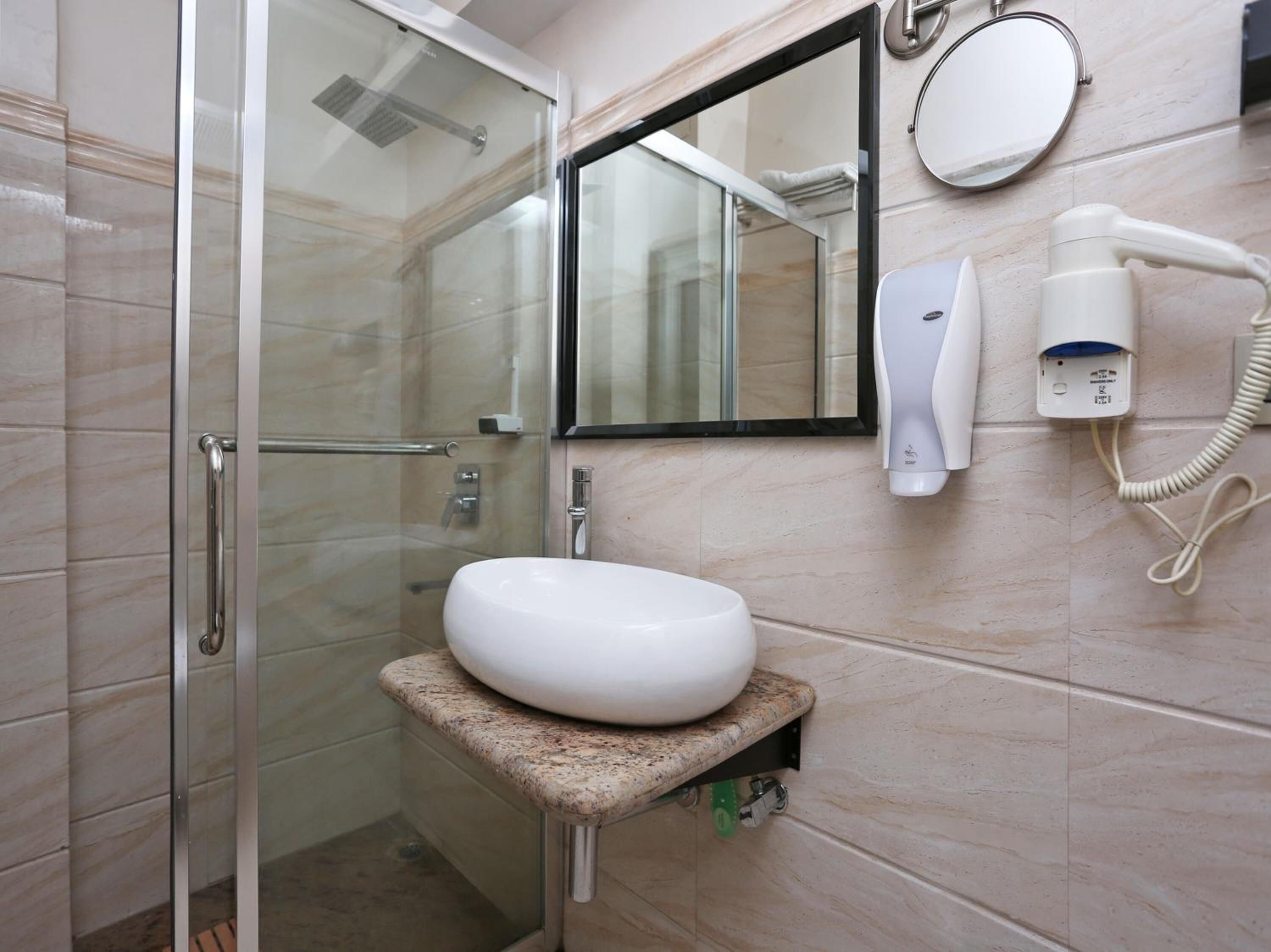 Une salle de bain avec une douche à parois de verre, un lavabo blanc, un miroir et un sèche-cheveux posé sur un support mural.