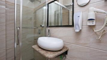 Une salle de bain avec une douche à parois de verre, un lavabo blanc, un miroir et un sèche-cheveux posé sur un support mural.