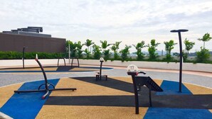 An outdoor exercise area with a blue and beige rubberized floor, exercise equipment, and a bench.