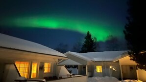 A house with a snow-covered roof and a view of the northern lights. - Lomavekarit (Rovaniemi)