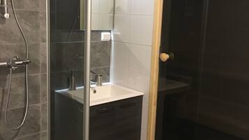 A modern bathroom with a glass shower enclosure, a white sink, and dark cabinetry.