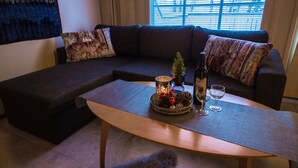 A modern living room with a sectional sofa, a coffee table with a decorative centerpiece, and a window with blinds. - Lomavekarit (Rovaniemi)