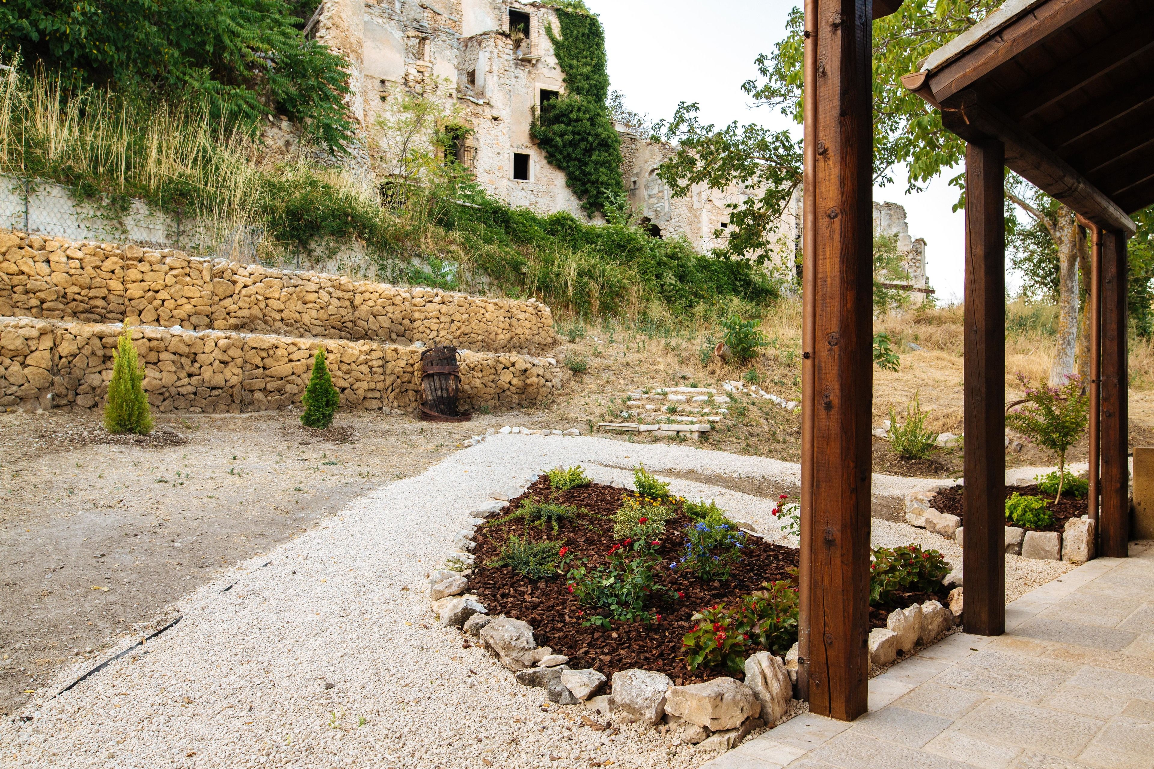 Eine Mauer aus Stein, ein Kiesweg und eine Holzpergola.