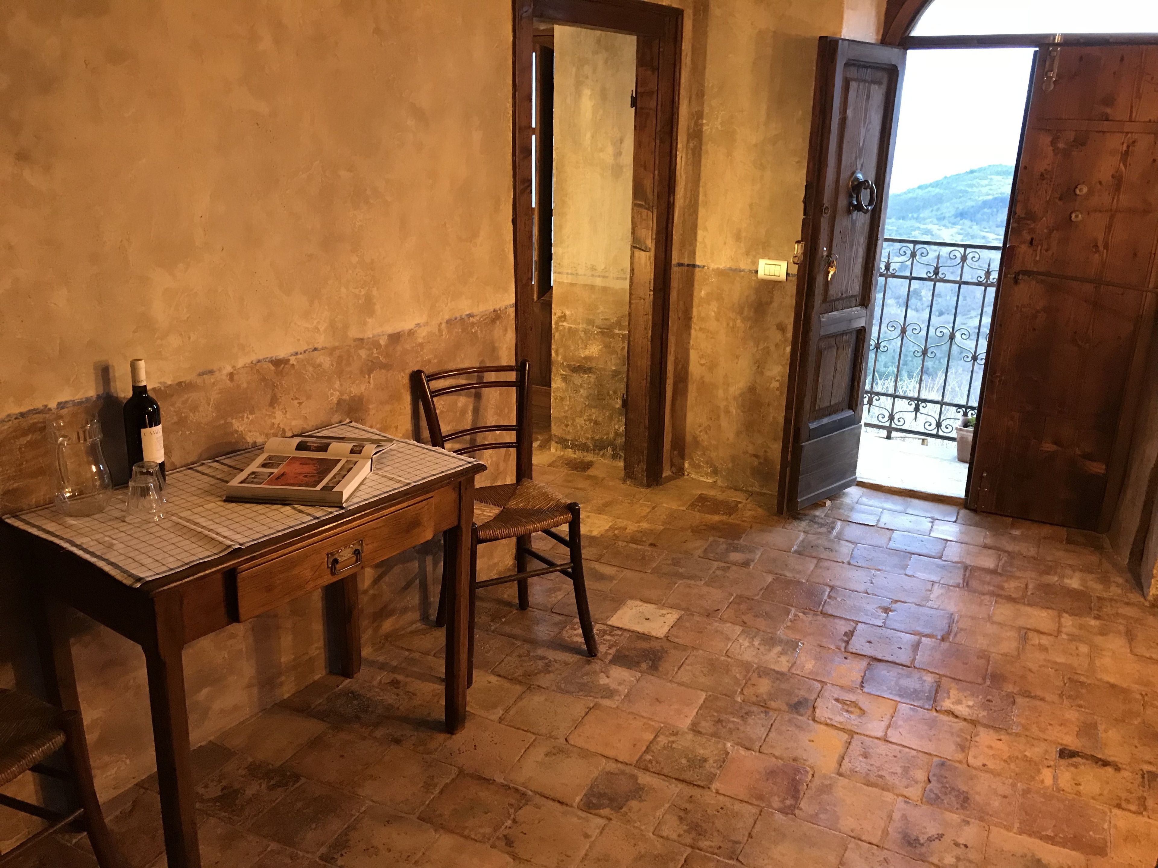 A rustic room with a wooden table, a chair, a wine bottle, and a book.
