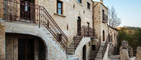 A stone building with a staircase leading to an upper level, featuring wrought iron railings and arched doorways.