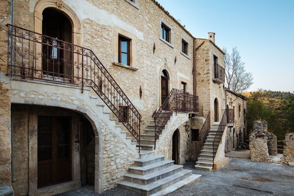 A stone building with a staircase leading to an upper level, featuring wrought iron railings and arched doorways.