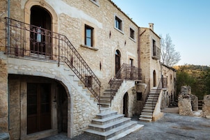 Un edificio de piedra con una escalera que conduce a un nivel superior, con barandillas de hierro forjado y puertas en arco.