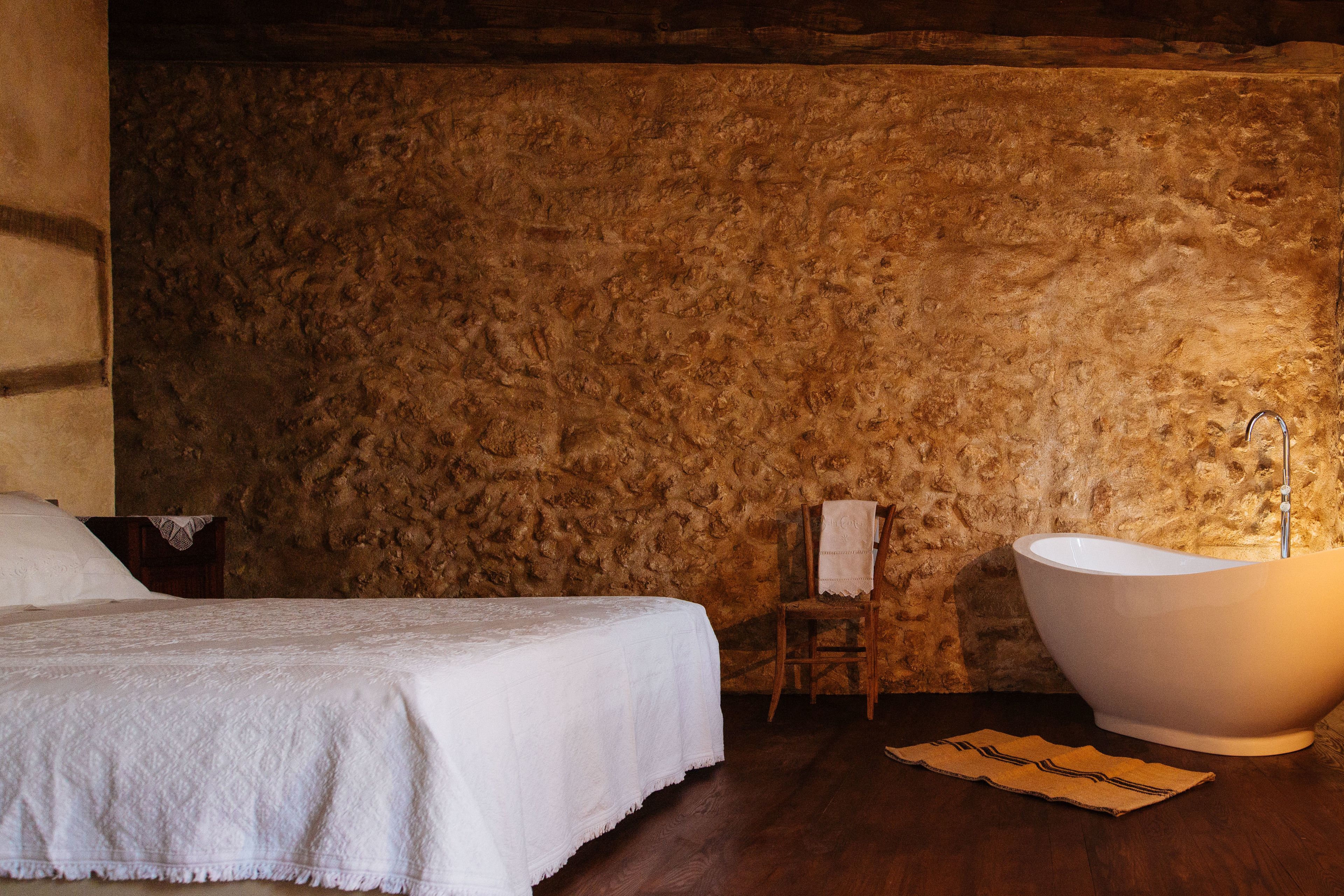 Een slaapkamer met een groot bed, een badkuip en een stenen muur.