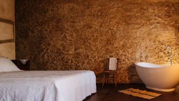 Een slaapkamer met een groot bed, een badkuip en een stenen muur.