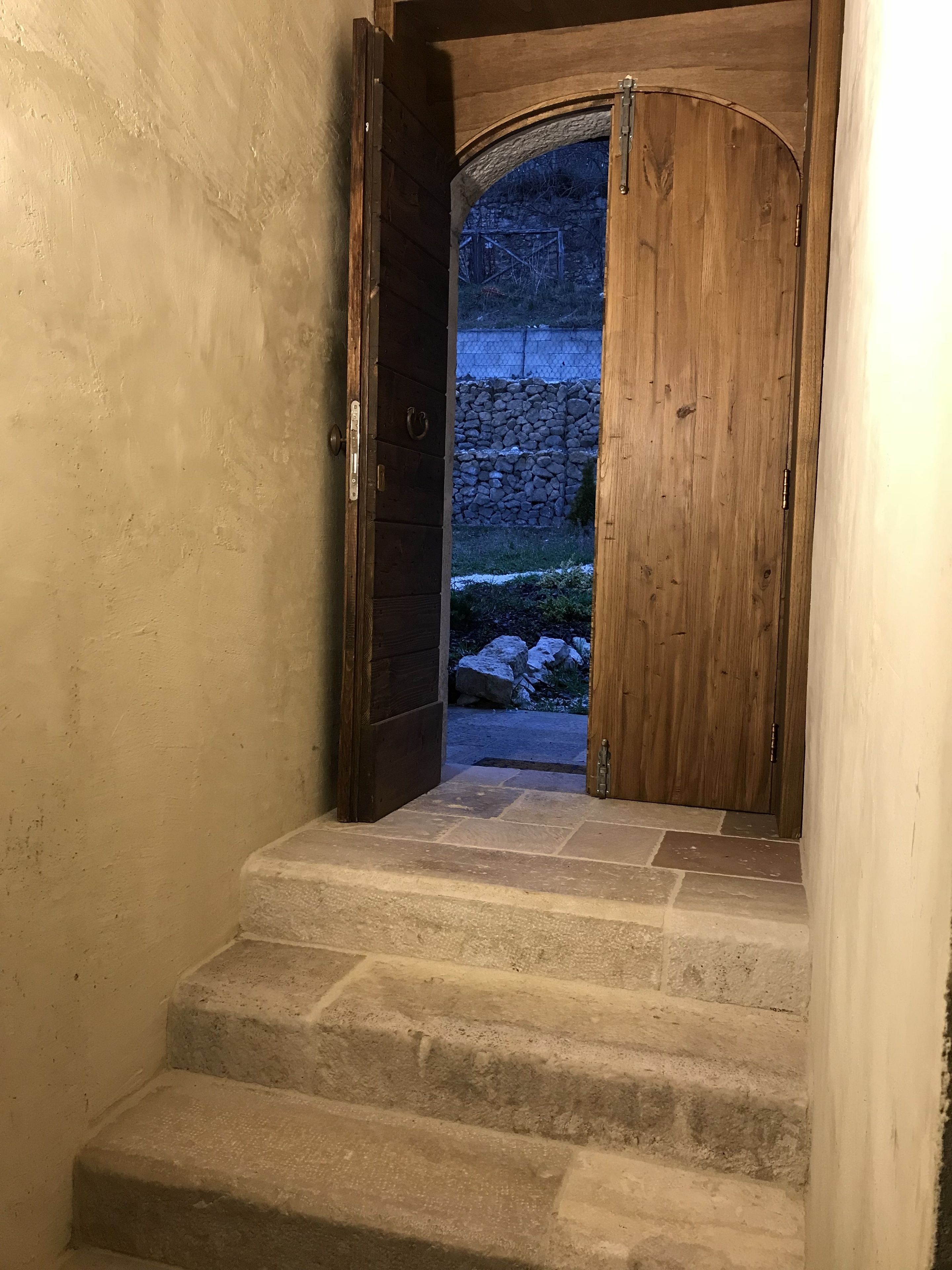 Uma porta de madeira com um arco de pedra que dá acesso a uma escadaria de pedra.