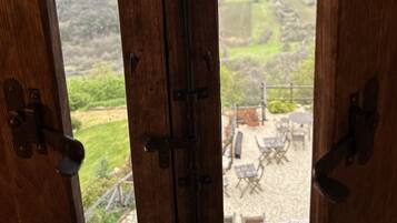 A wooden-framed window with a view of a green landscape and distant hills.