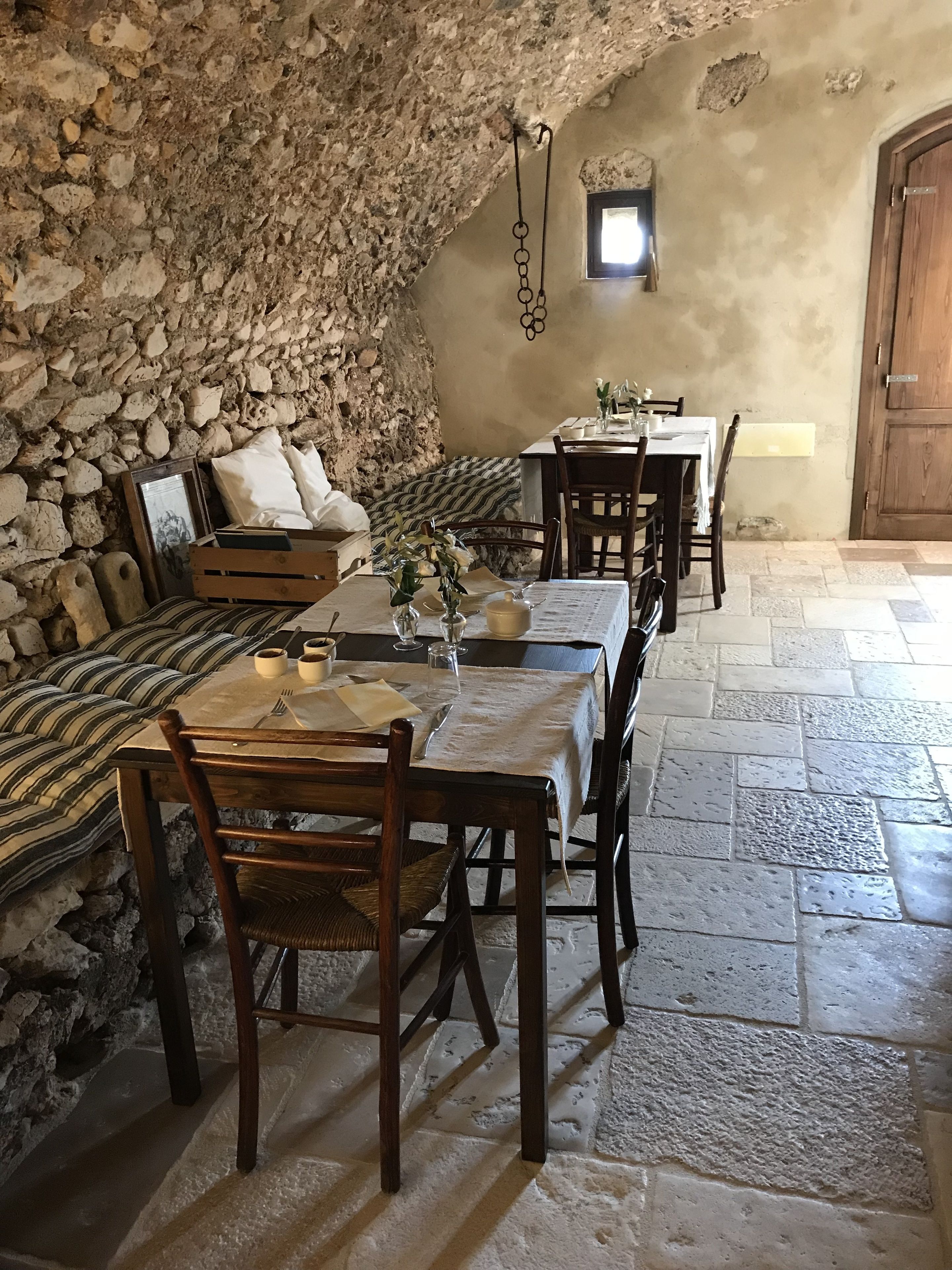 A rustic dining area with stone walls, wooden furniture, and a stone floor.
