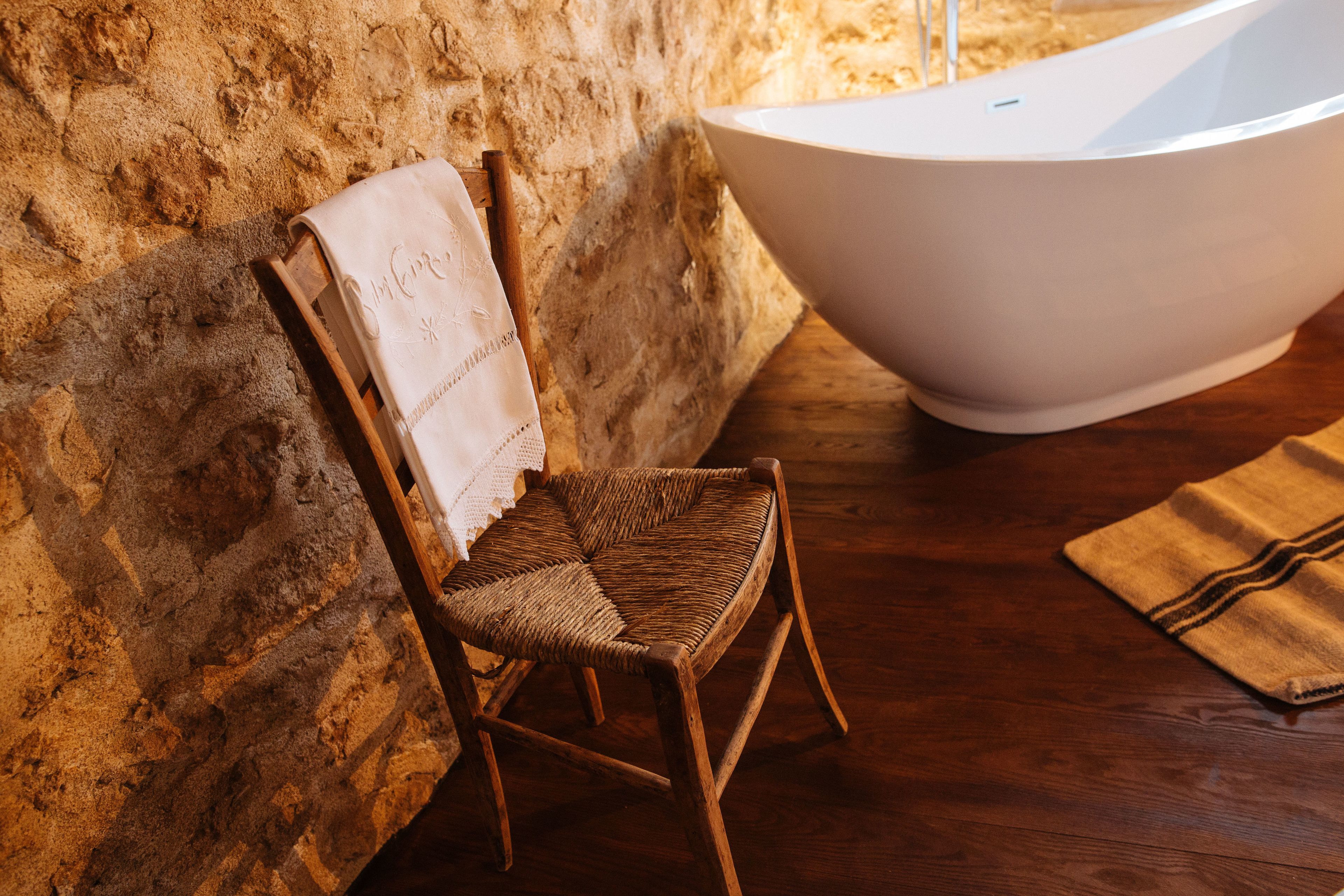 A wooden chair with a towel draped over its back, a white bathtub, and a wooden floor.