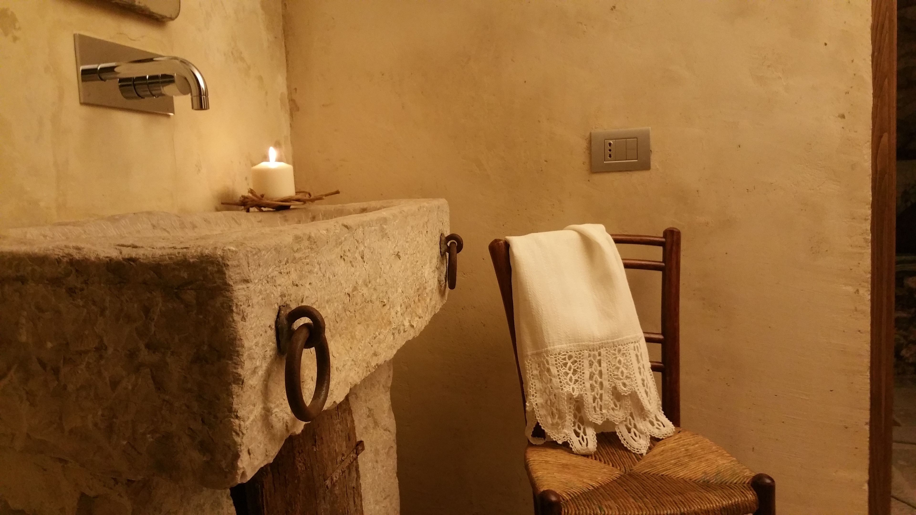 Ein Badezimmer mit einem Steinkreuz, einer brennenden Kerze, einem hölzernen Stuhl mit weißem Bezug und einem an der Wand befestigten Lichtschalter.