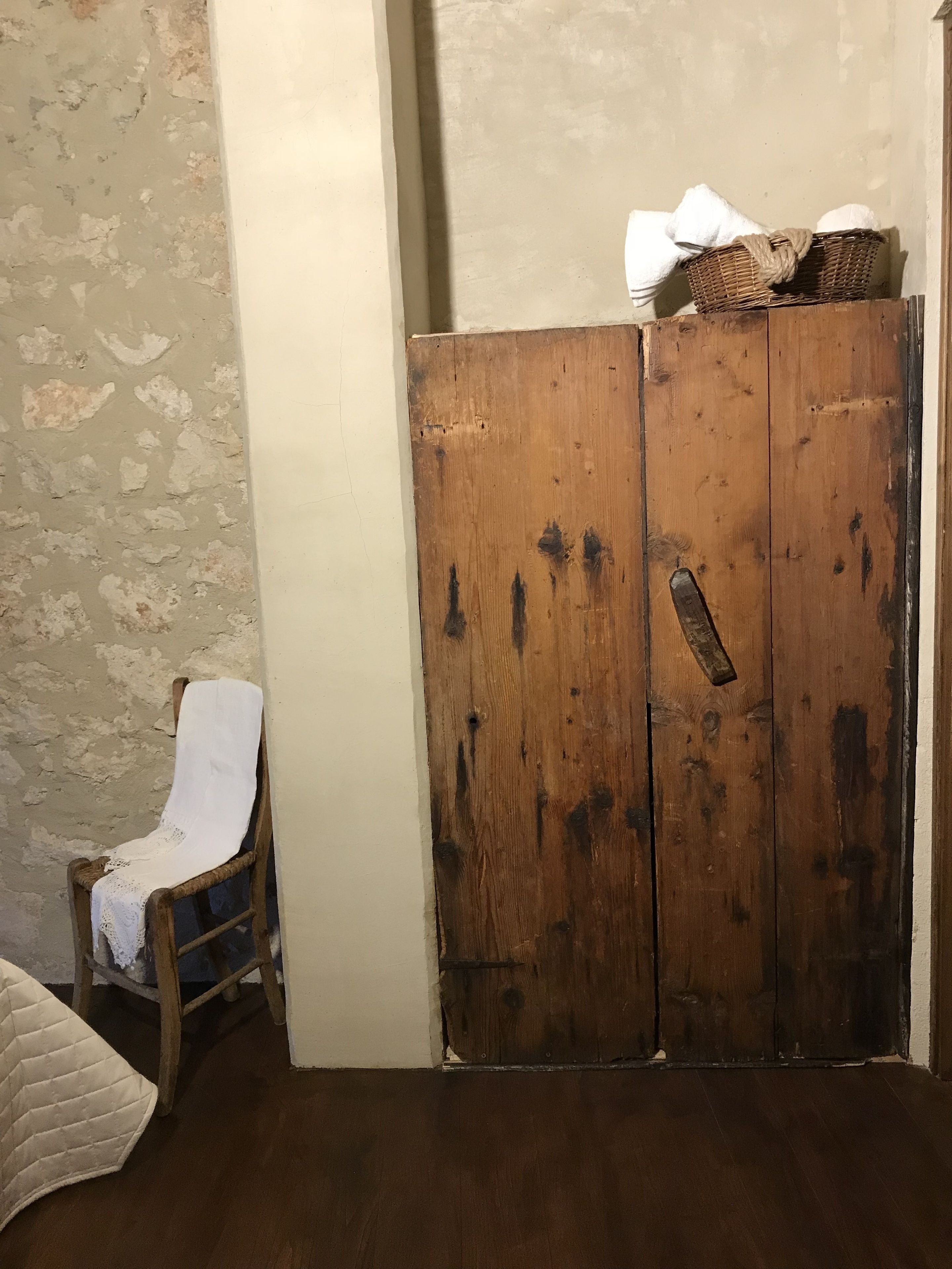 A room with a wooden wardrobe, a chair with a white cover, and a textured wall.