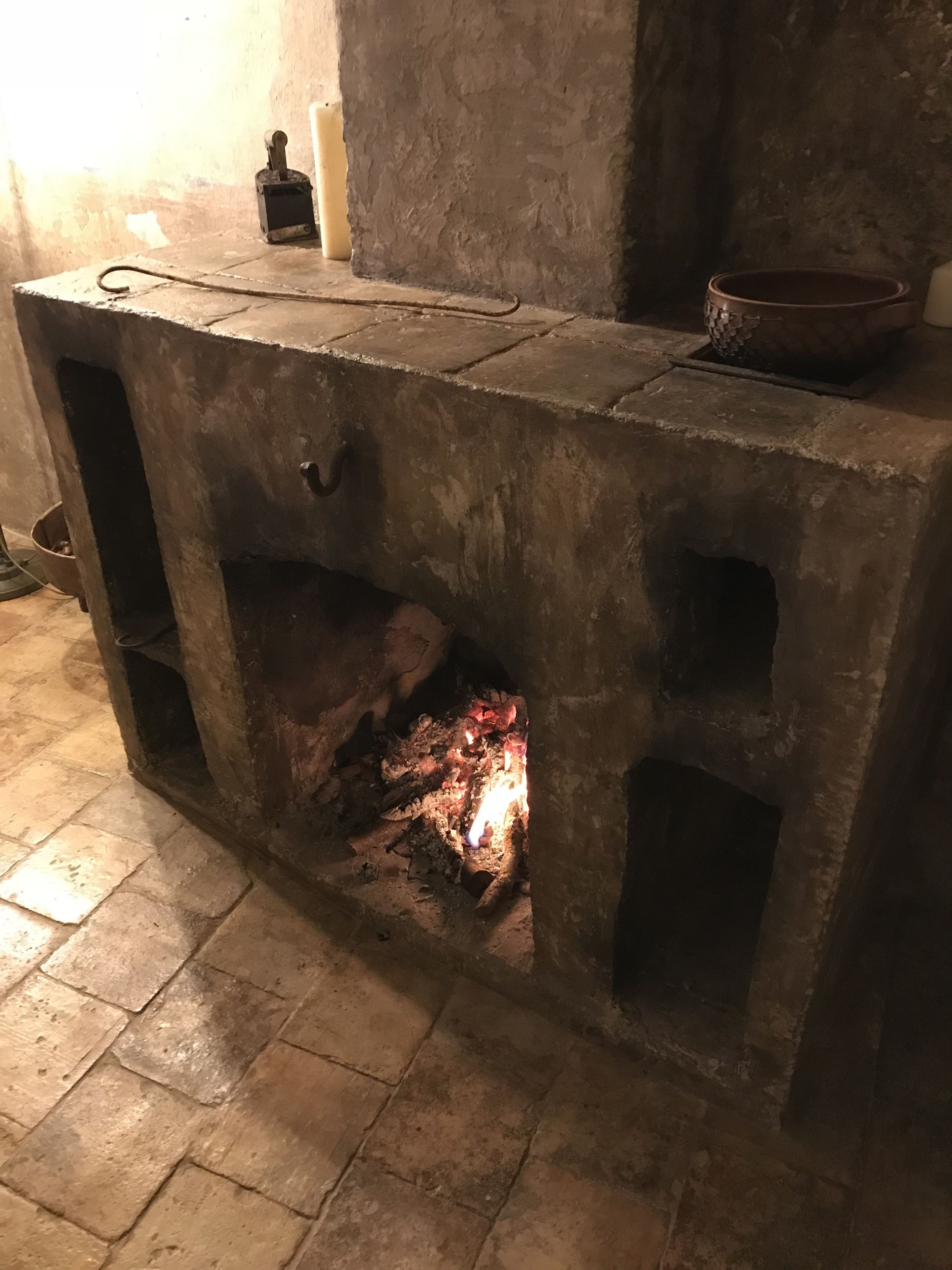 Una llar de pedra amb foc encès a l'interior, un bol a la part superior i una finestra petita a l'esquerra.