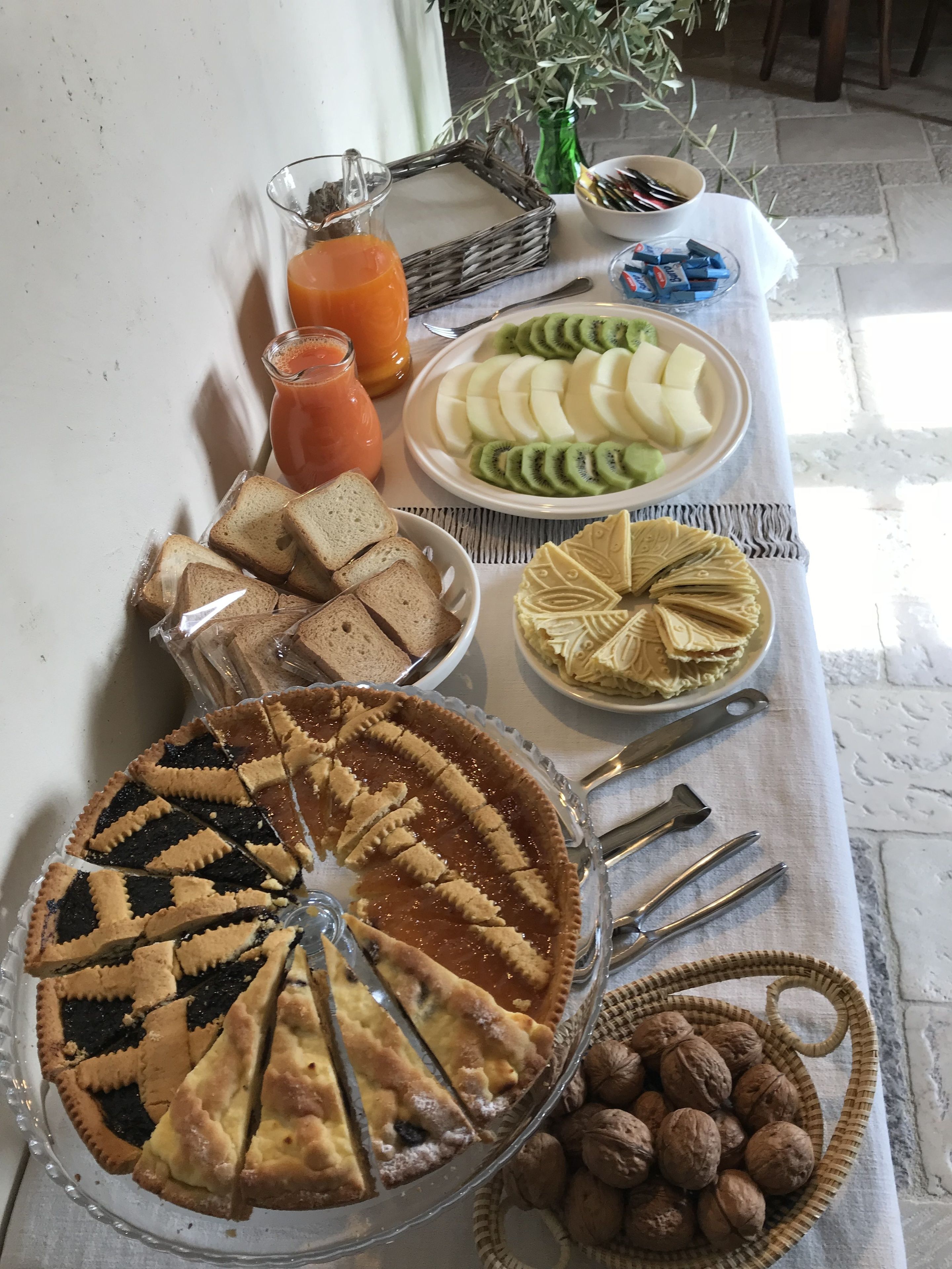A table with a variety of food items including a pie, sliced fruits, sandwiches, and nuts.