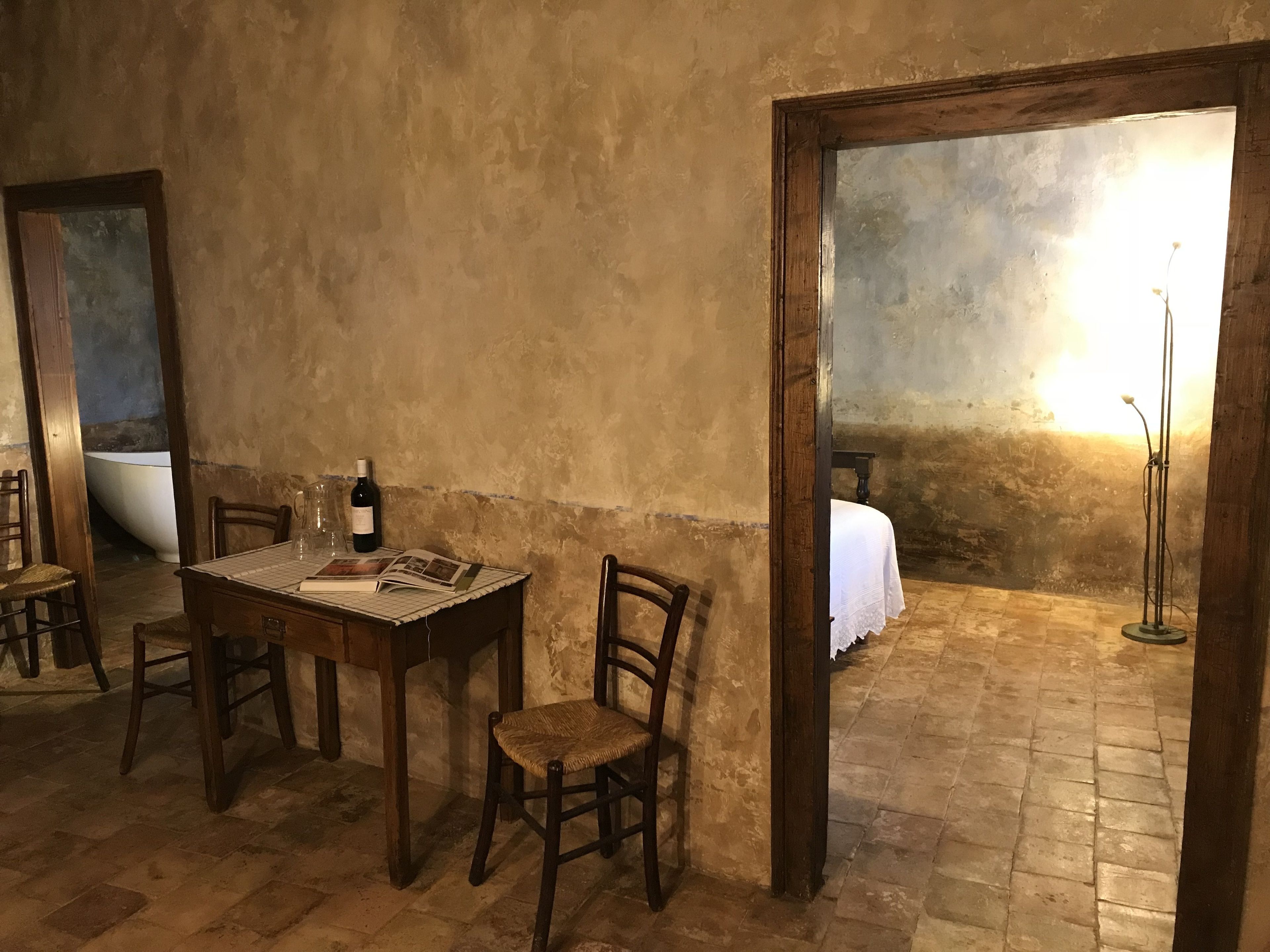 A rustic dining area with a wooden table, chairs, and a wine bottle.
