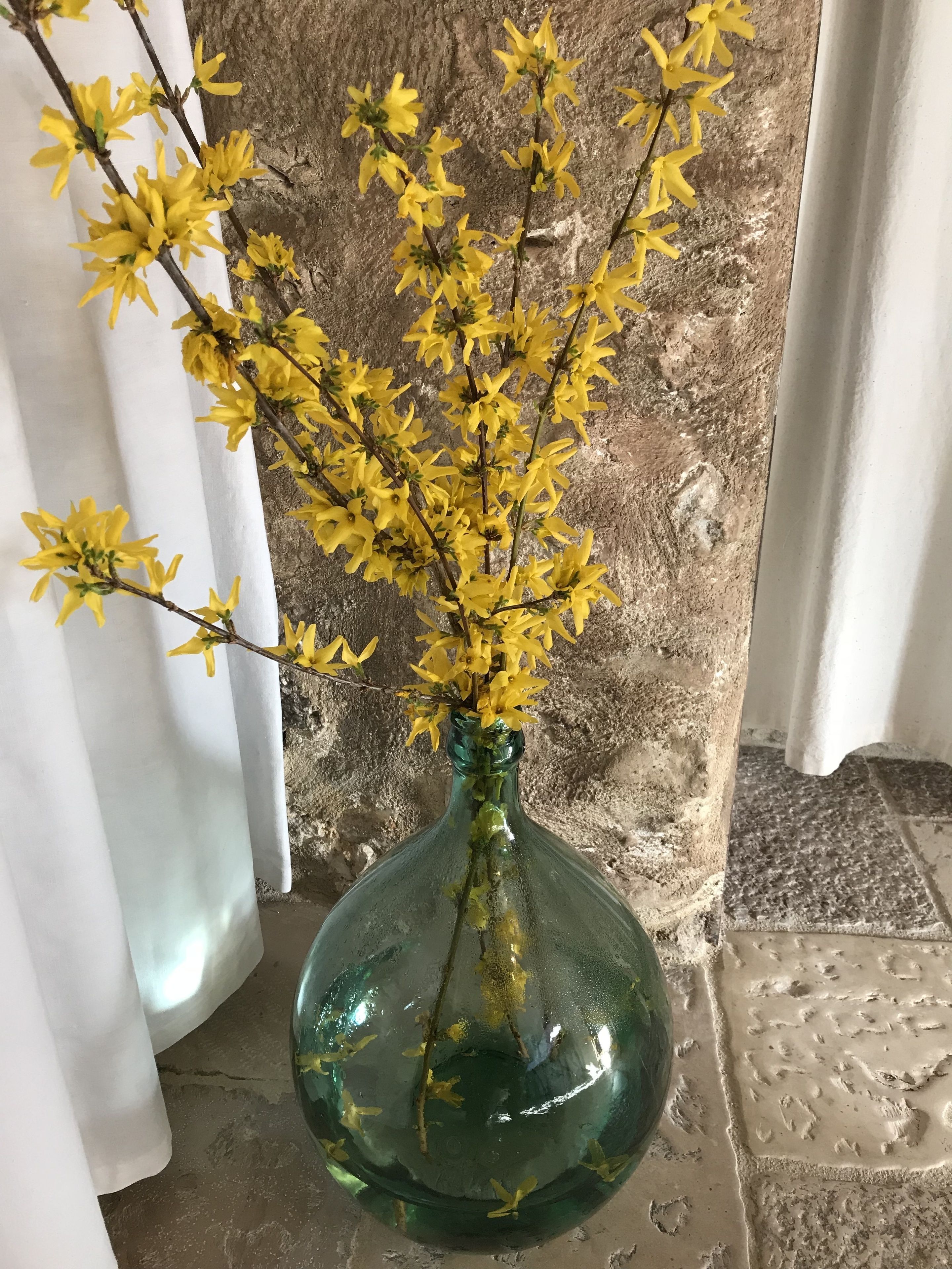 Un jarrón verde con flores amarillas sobre una pared de piedra.