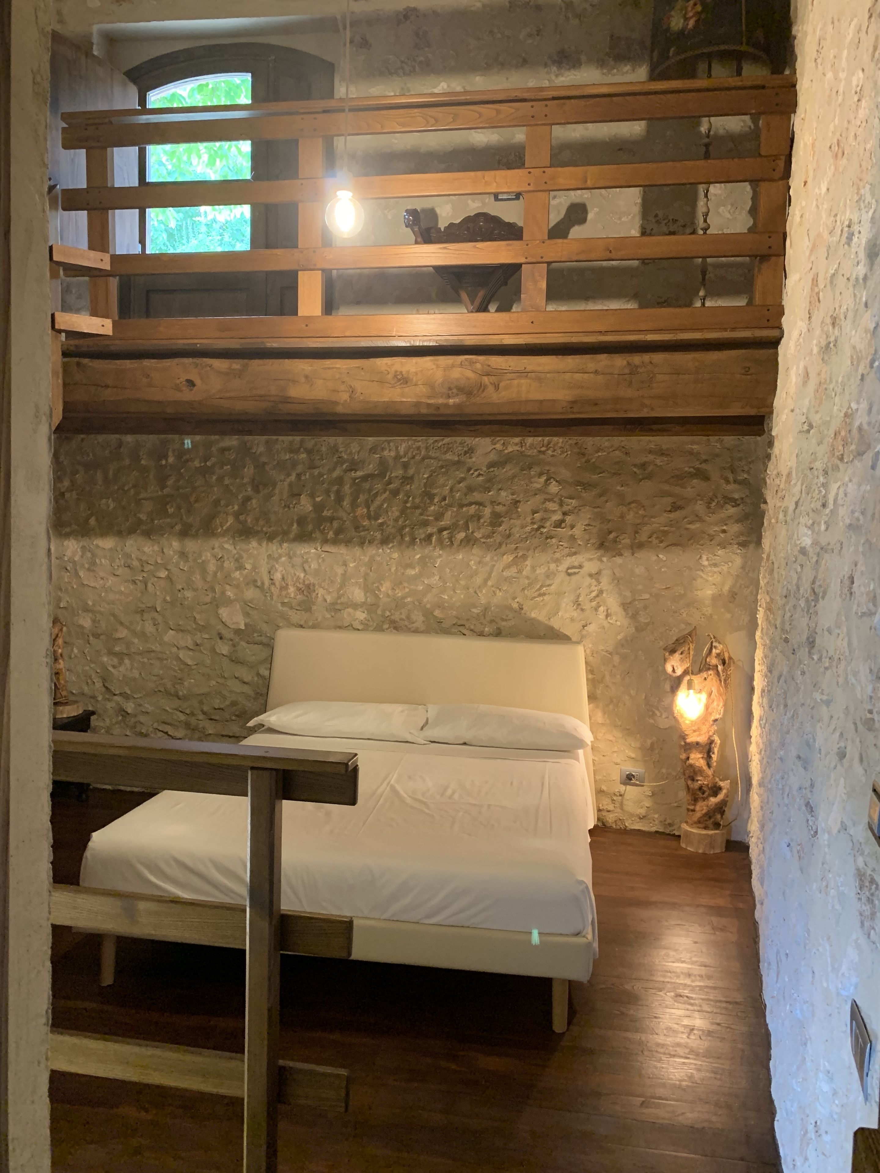 Ein Schlafraum mit Etagenbett, einer rustikalen Steinwand, einem Holz-Kopfteil und einer Nachttischlampe.