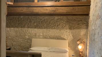 Ein Schlafraum mit Etagenbett, einer rustikalen Steinwand, einem Holz-Kopfteil und einer Nachttischlampe.
